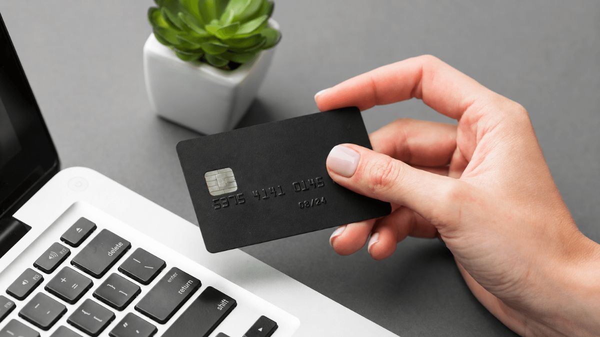 Person holding a black credit card next to a laptop before paying a service deposit