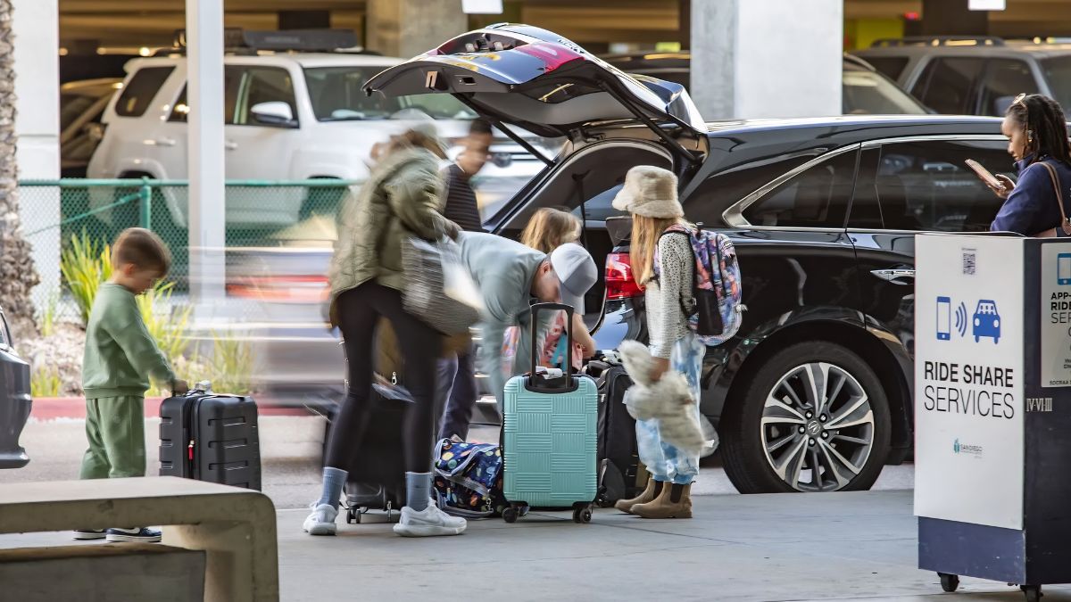 A family loading luggage into the trunk of a rideshare vehicle next to a designated pickup sign.