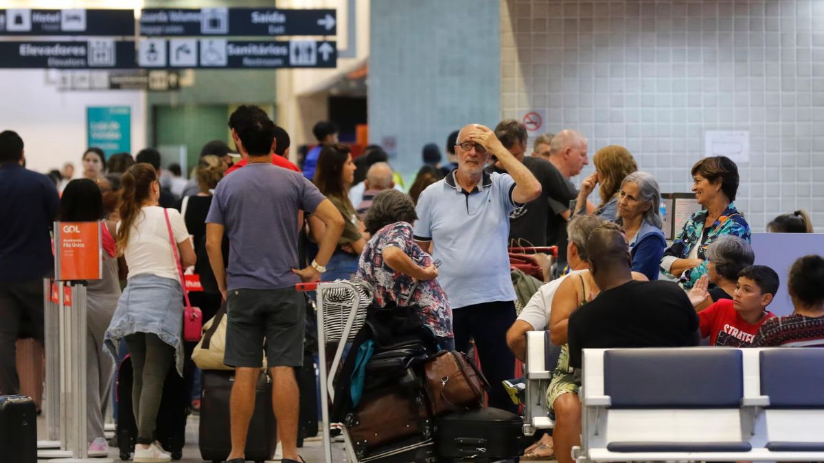 A crowded airport terminal filled with travelers and luggage, featuring a man holding his head in frustration due to travel delays.