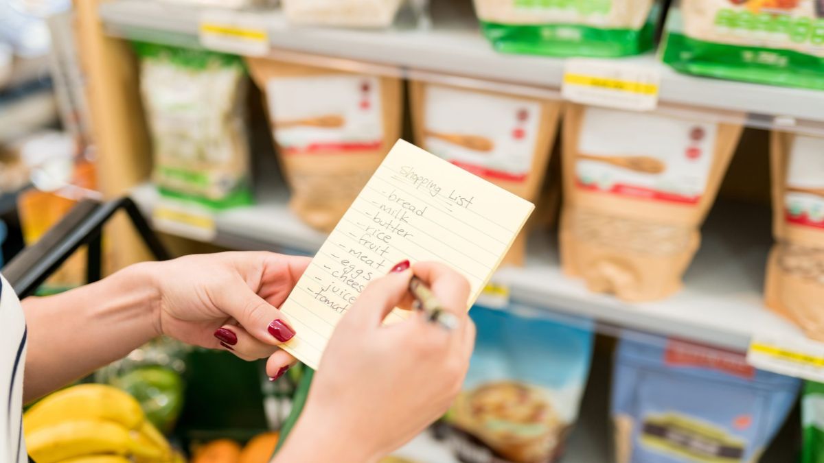 A shopper holding a handwritten shopping list inside a grocery store aisle stocked with packaged foods, highlighting considerations for Spanish-language labels in San Ysidro.
