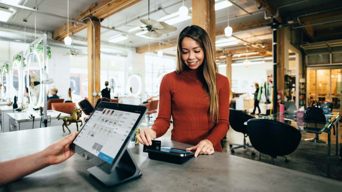Store employee smiling while processing a customer's contactless payment on a modern tablet POS system at the checkout counter of a small business