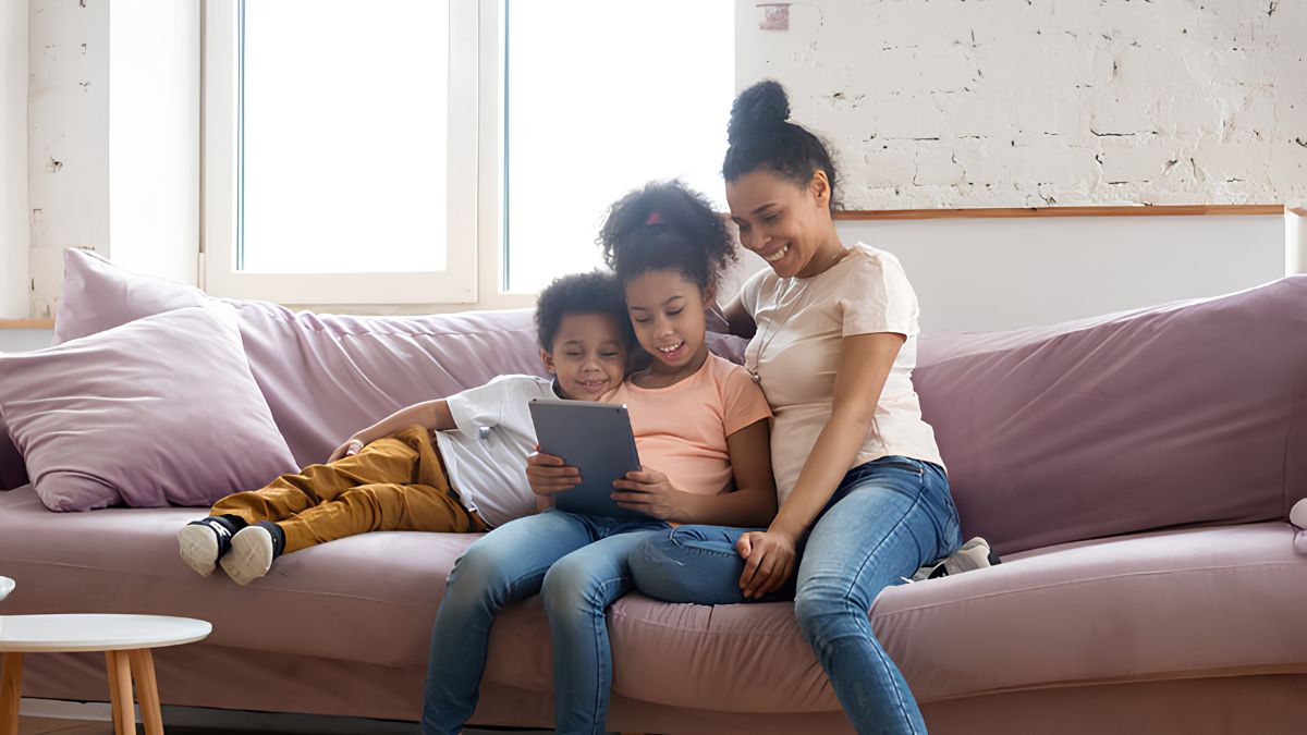 A mother and two children sitting together on a couch while looking at a tablet screen