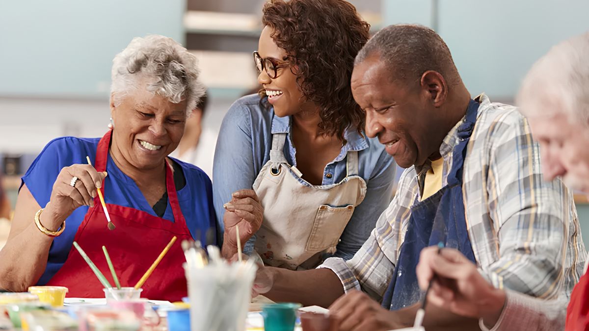 An instructor smiling with older adults participating in a painting art class
