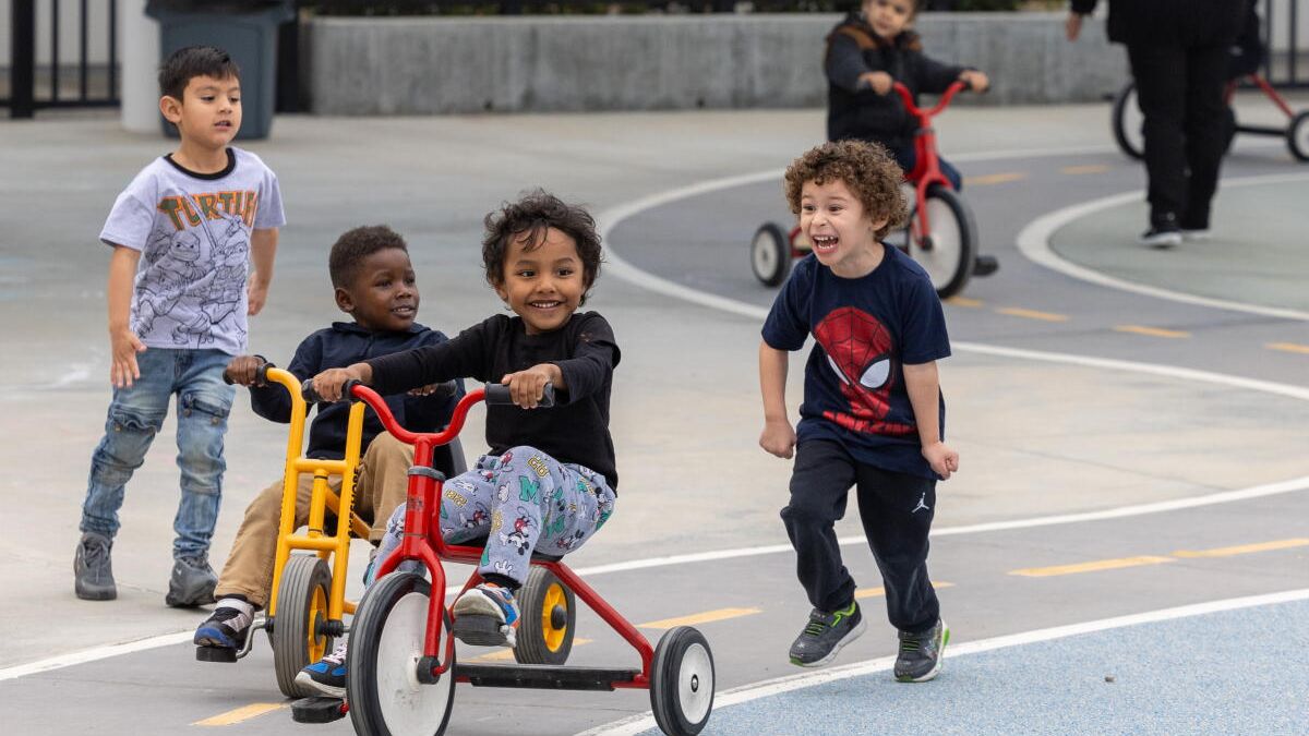 Young children smiling and having fun riding tricycles and playing at an outdoor recreation area, illustrating youth activities in San Ysidro.