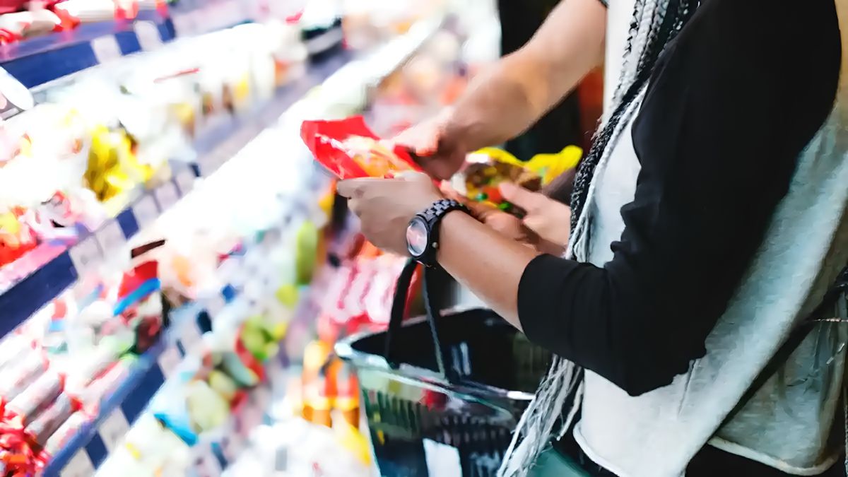 A shopper inspecting a packaged food item while browsing grocery store shelves.