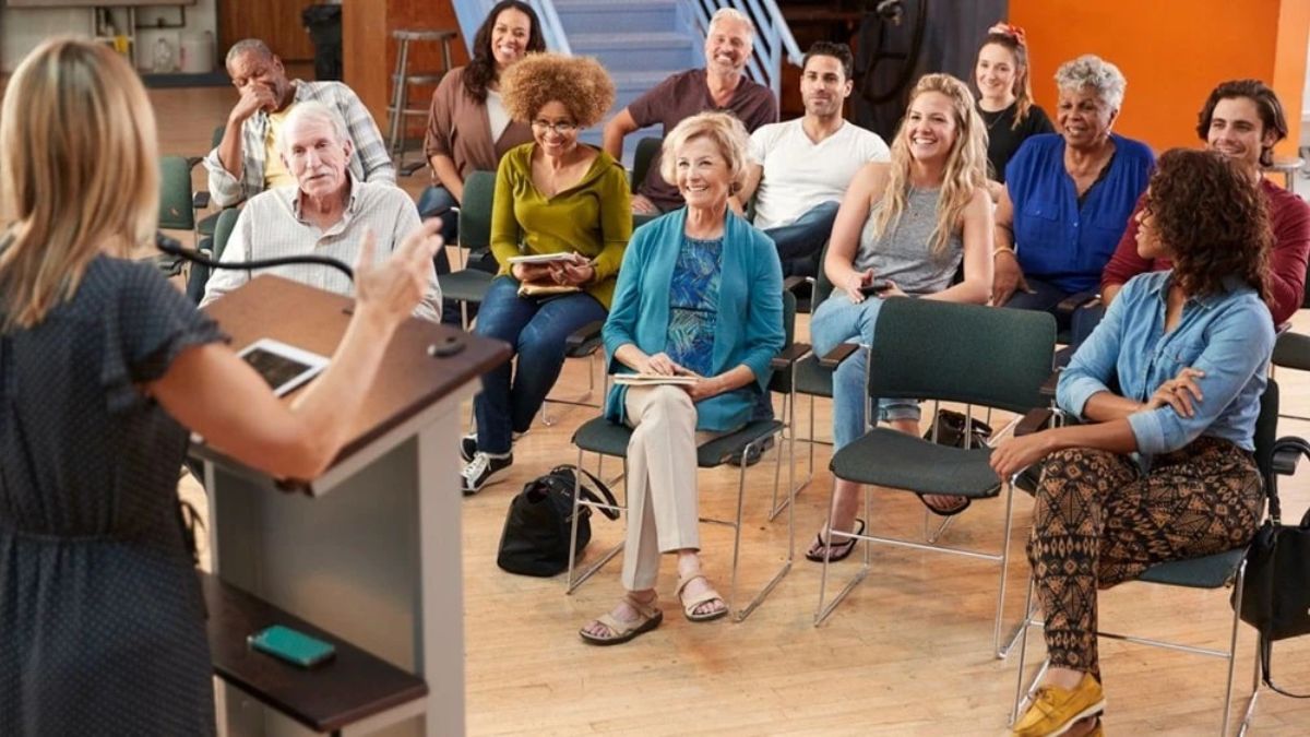 A speaker presenting to a diverse group of attentive audience members seated in a community room.