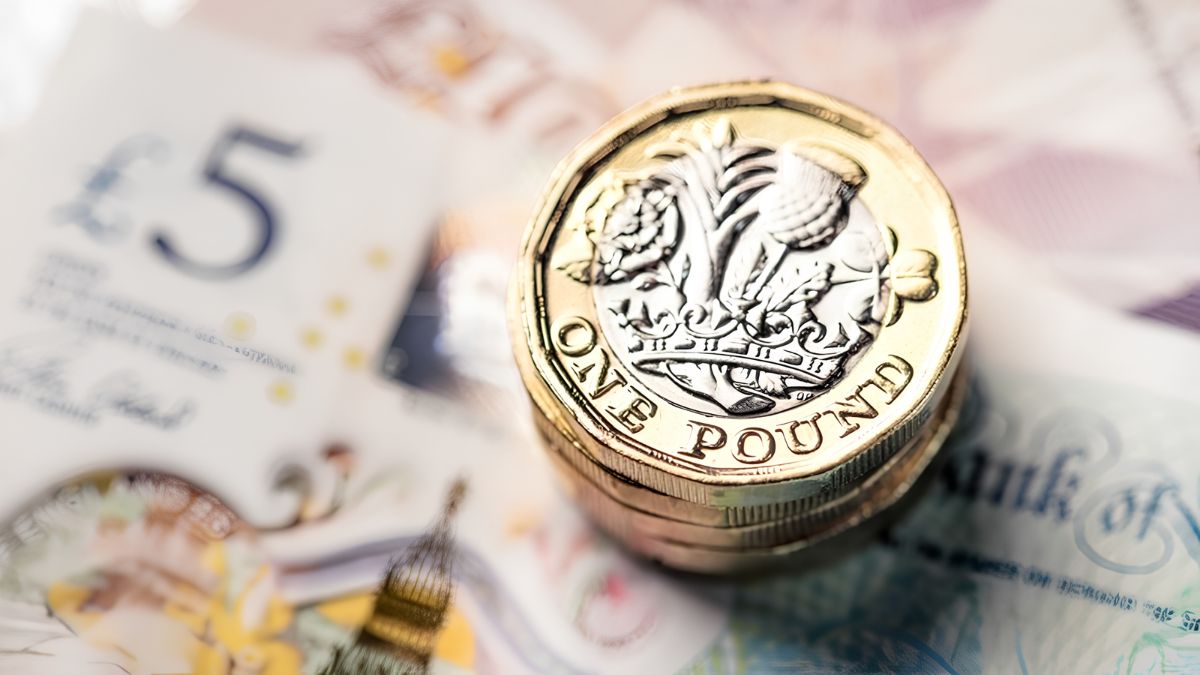 A stack of British One Pound coins resting on top of British pound banknotes, symbolizing financial cost-cutting and business savings