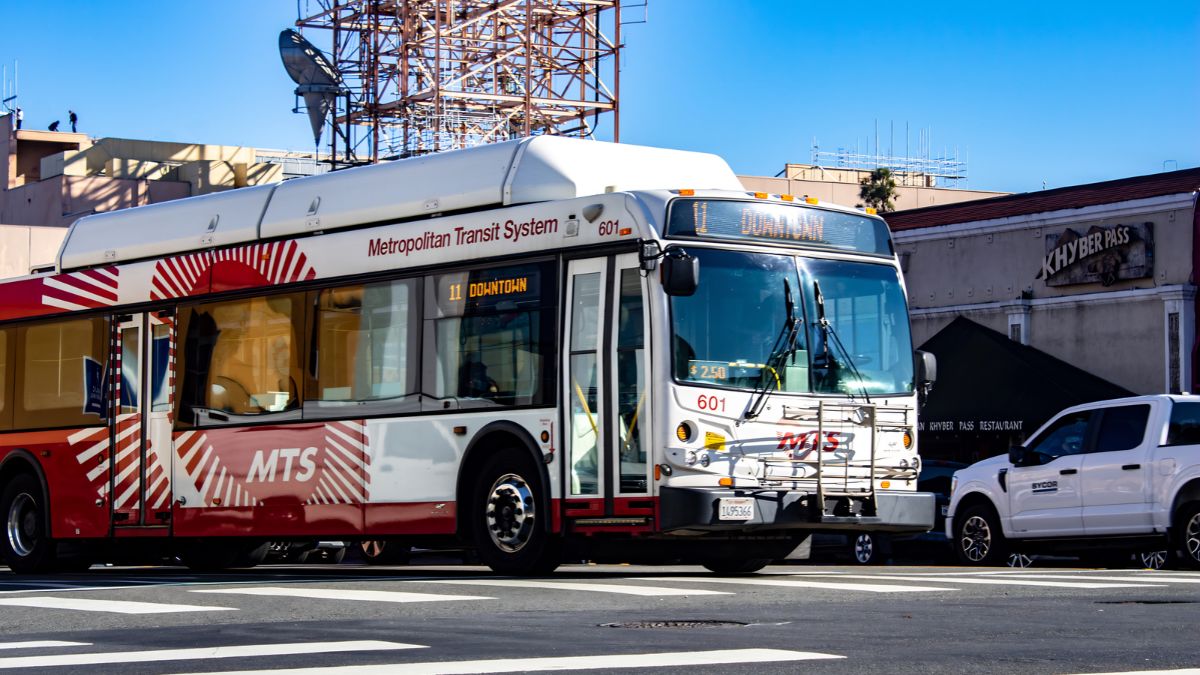 A red and white Metropolitan Transit System (MTS) bus traveling along a city street in San Ysidro