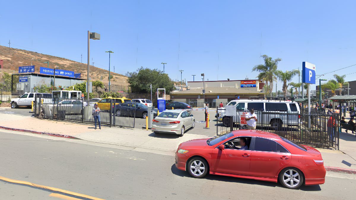 An outdoor street view of a neighborhood area in San Ysidro featuring parked cars, pedestrians, and local commercial buildings.