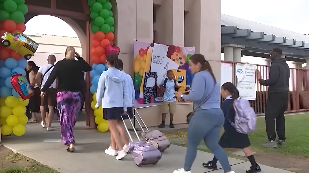 Parents and students arriving at a school entrance decorated with colorful balloons and a back-to-school banner.
