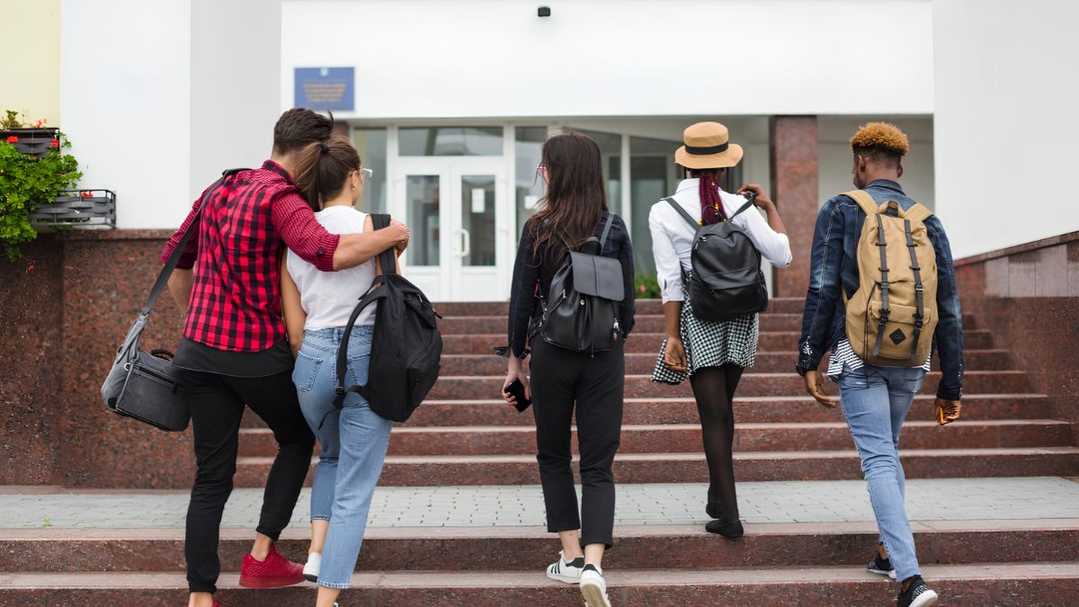A diverse group of young adults carrying backpacks and walking up a flight of steps together outside a building