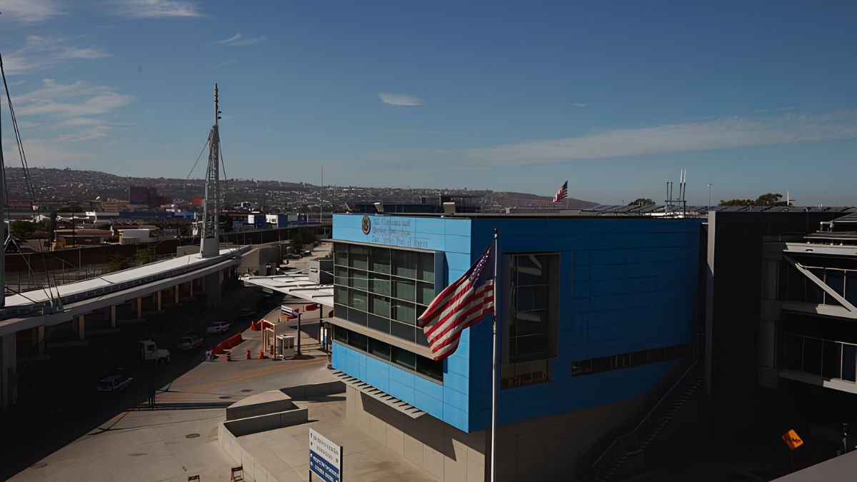An American flag flying in front of a modern blue public building and urban infrastructure in San Ysidro.