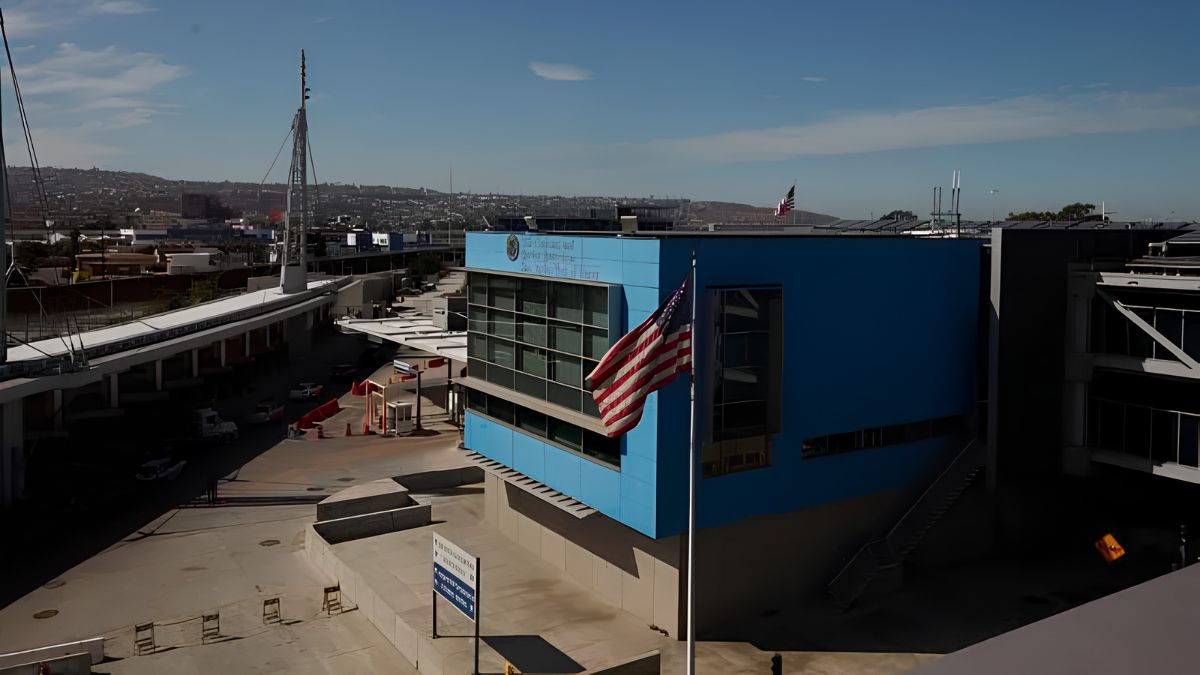 An American flag flying in front of the modern San Ysidro border crossing facility and surrounding infrastructure development