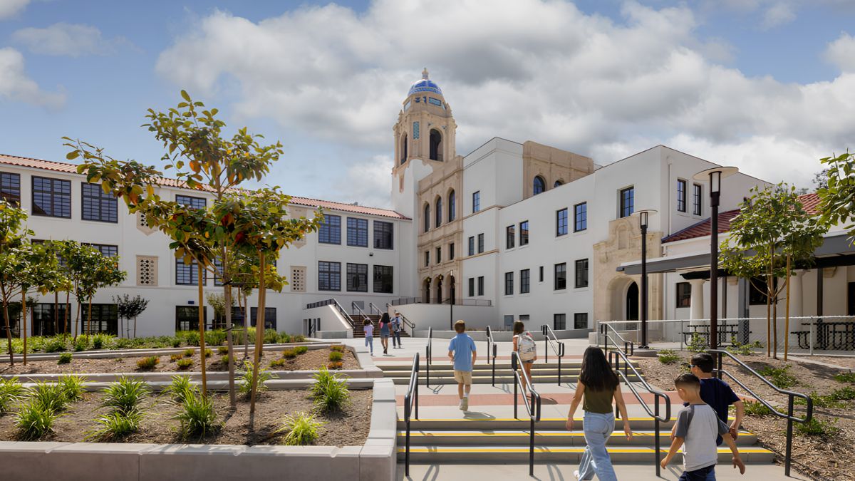 Children walking down outdoor stairs in a school courtyard in front of a white architectural building with a distinctive tower