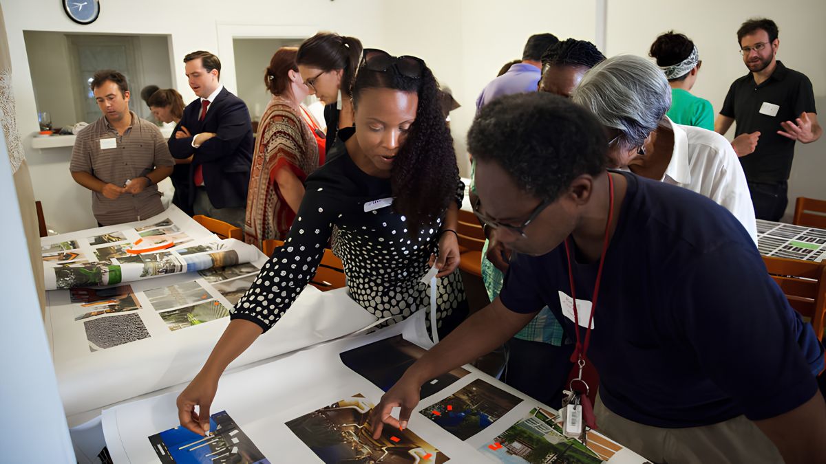 A diverse group of community members collaborating around a large table, reviewing and planning documents together indoors.