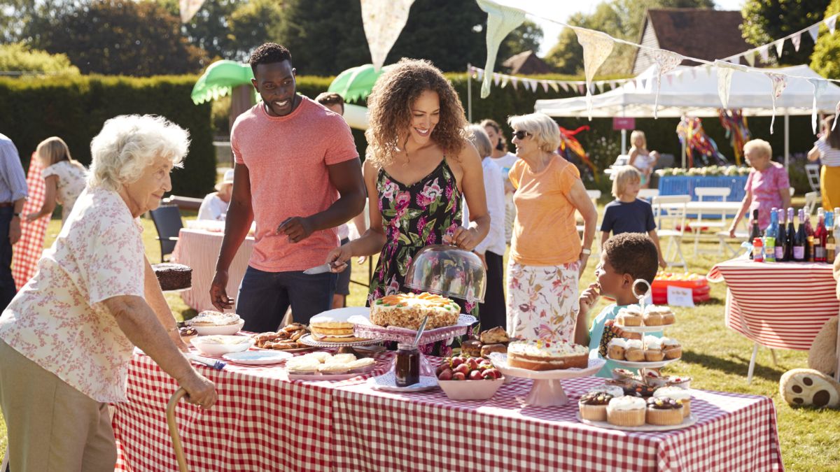 Diverse community members enjoying a outdoor fundraising event and bake sale setup with tables full of food.