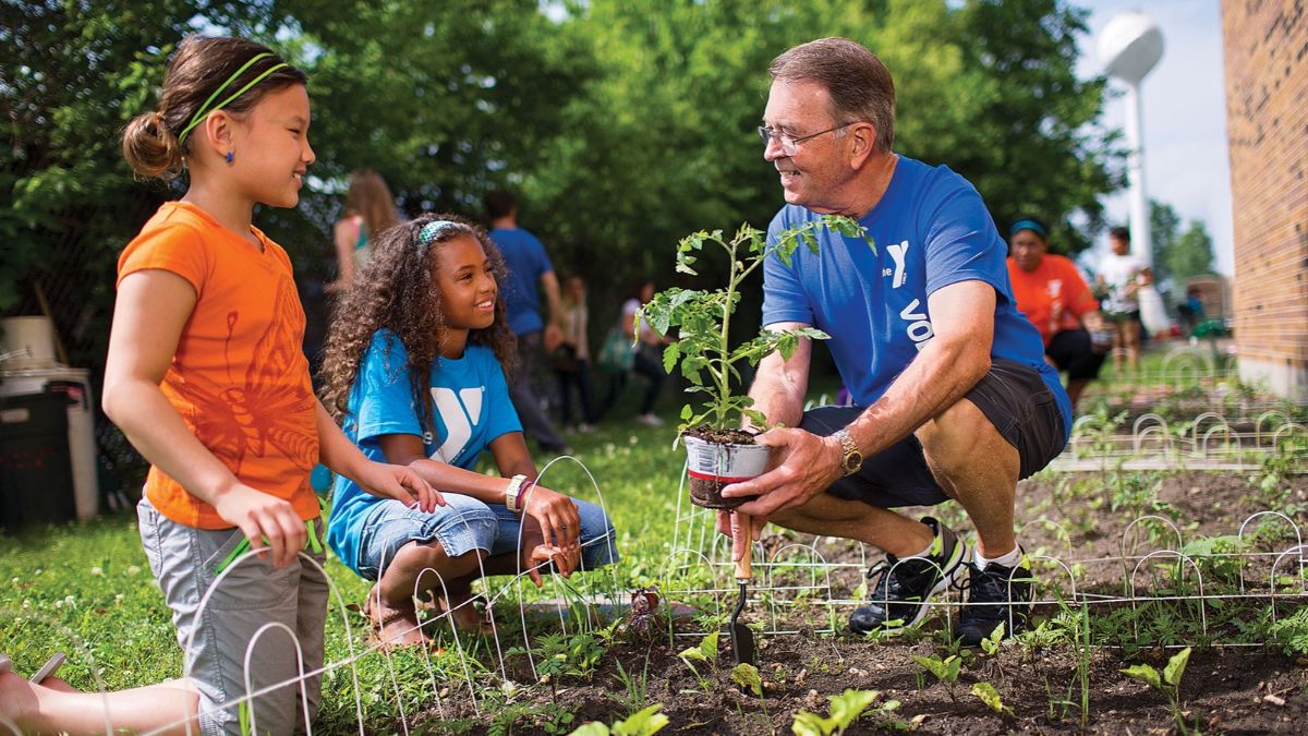 Smiling volunteer mentor planting a seedling with two young girls in an outdoor community garden project