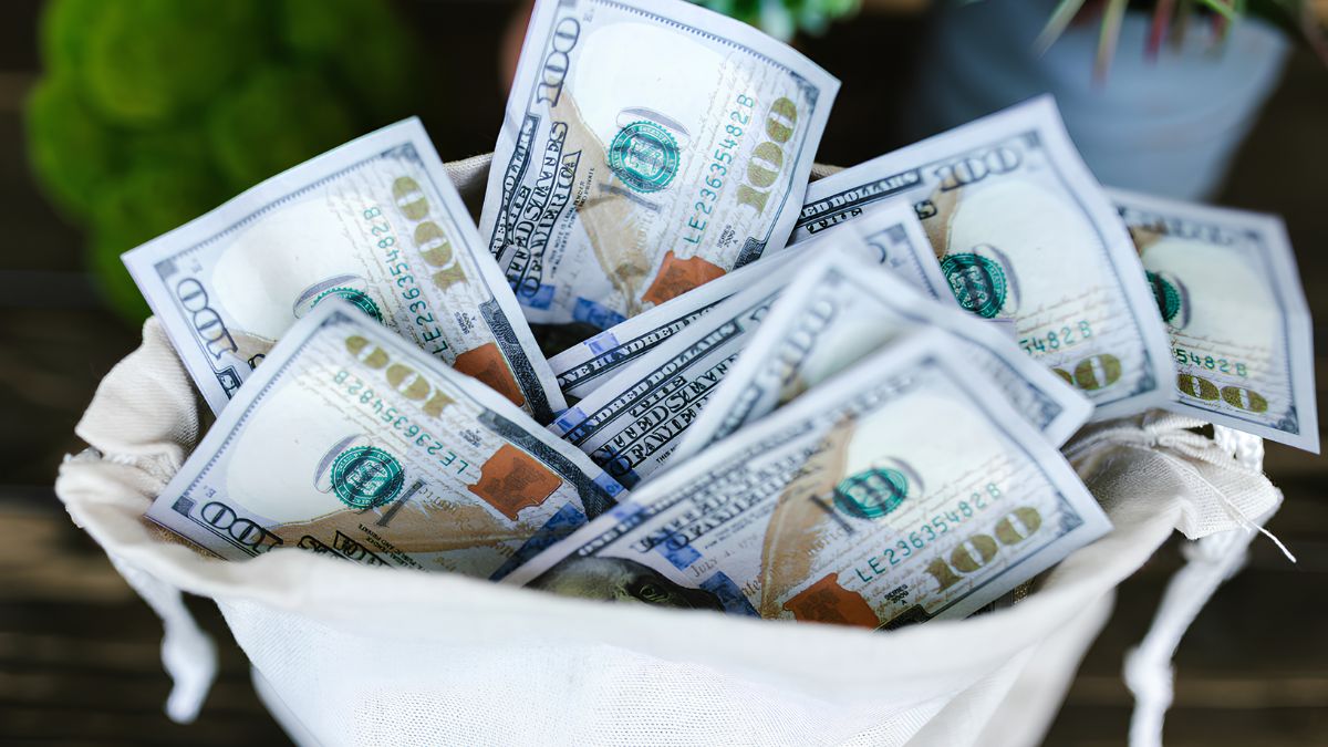 A cloth bag filled with a stack of one hundred dollar bills representing household savings and budgeting in San Ysidro.