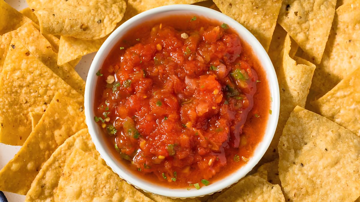 A white bowl of fresh red salsa surrounded by crunchy tortilla chips