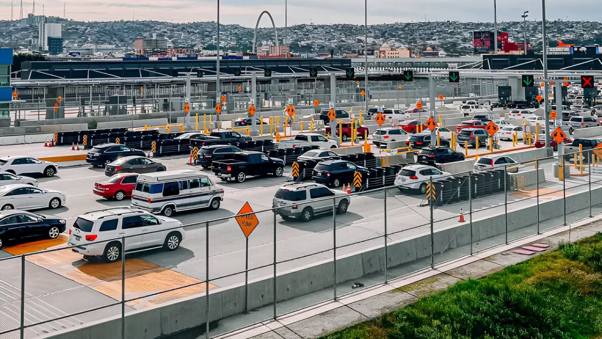An aerial view of cars and vehicles lined up at a busy border crossing station with booths and traffic lanes.