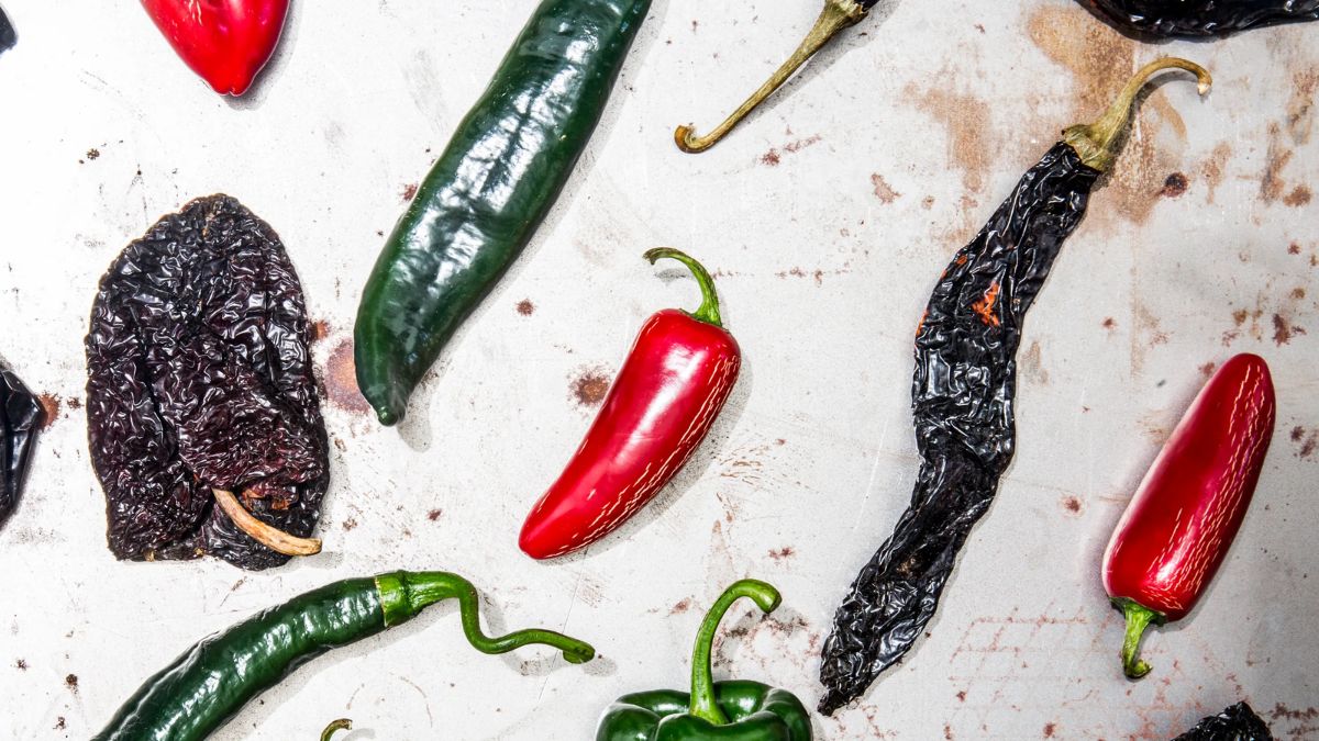 Flat lay view of various fresh and dried Mexican chiles arranged on a rustic light-colored surface