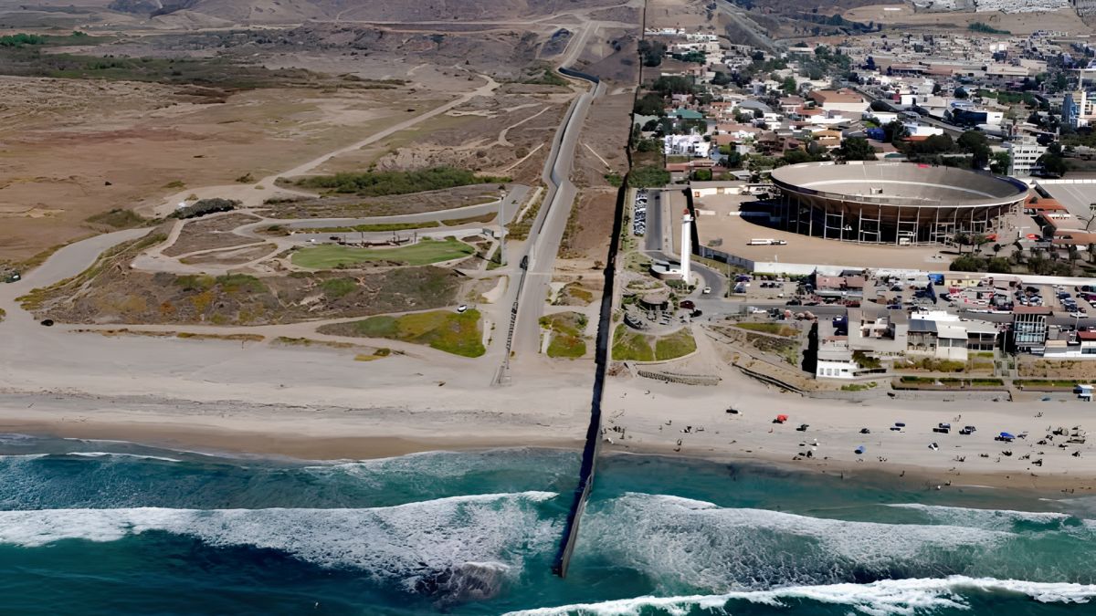 Aerial view of the US-Mexico border fence extending into the Pacific Ocean, separating the coastal landscapes near San Ysidro and Tijuana.