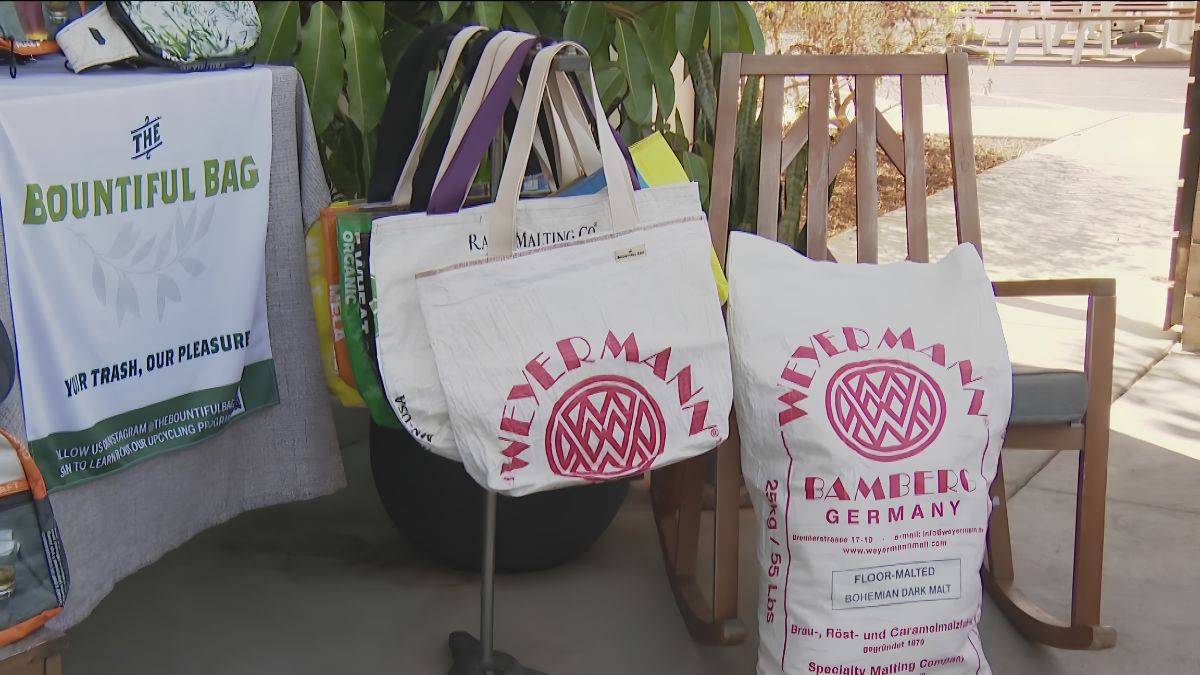Display of branded fabric tote bags and a Weyermann malt bag at a local market or storefront booth setup.