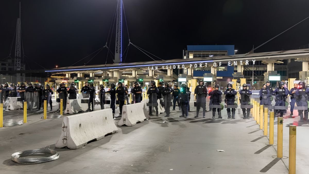 Nighttime view of the San Ysidro Port of Entry featuring security personnel and barrier installations