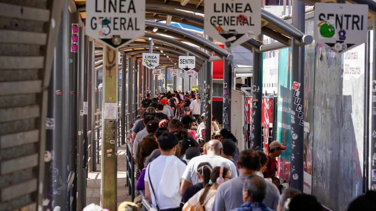 Crowd of travelers waiting in line at the San Ysidro border crossing under overhead signs marked 'Linea General' and 'SENTRI'