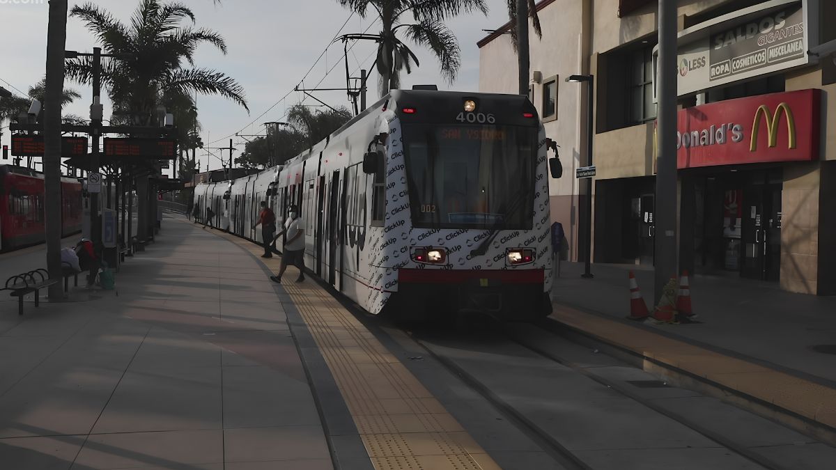 A San Diego Trolley light rail train stopped at a station platform in San Ysidro near a McDonald's restaurant.