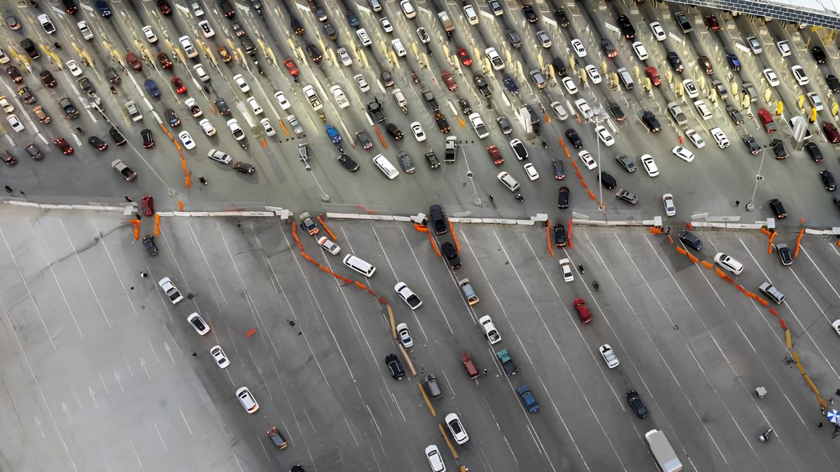 Aerial overhead view of multiple vehicle lanes lined with cars at the San Ysidro border crossing.