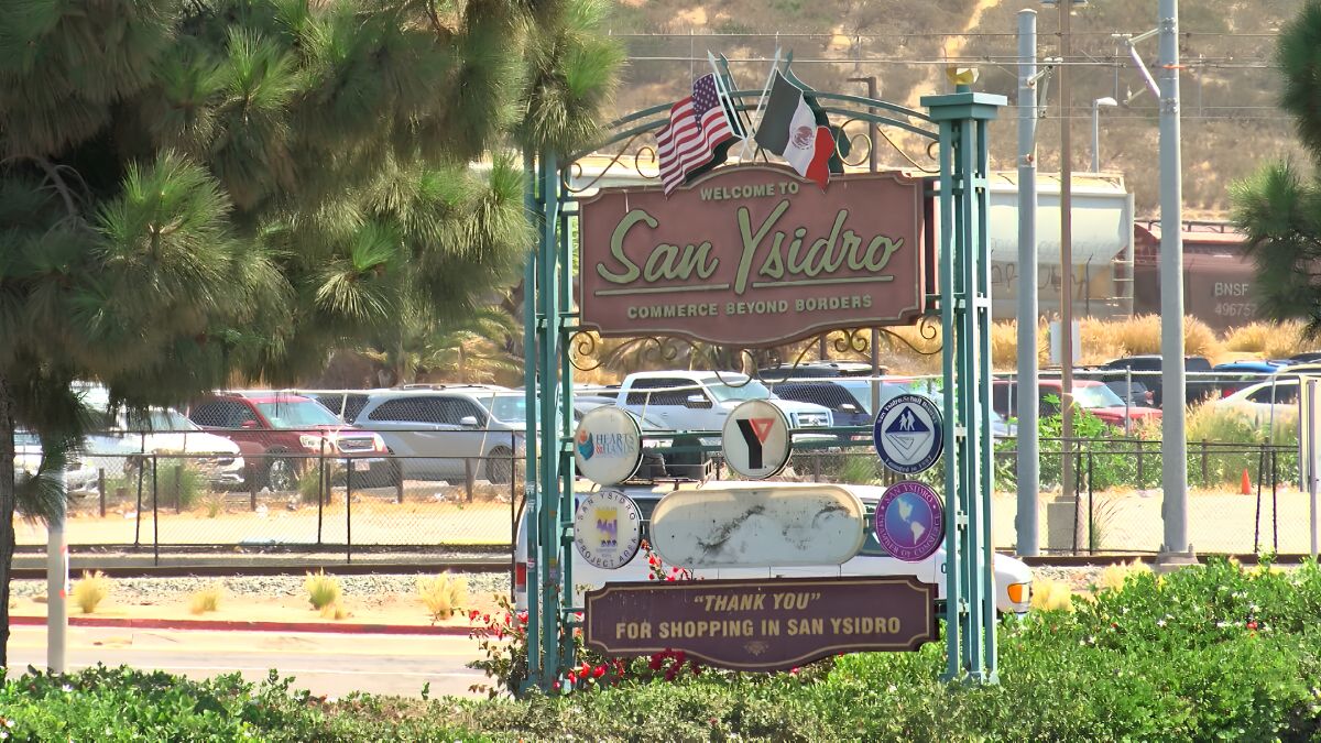 A decorative community welcome sign reading "San Ysidro: Commerce Beyond Borders" with American and Mexican flags on top.