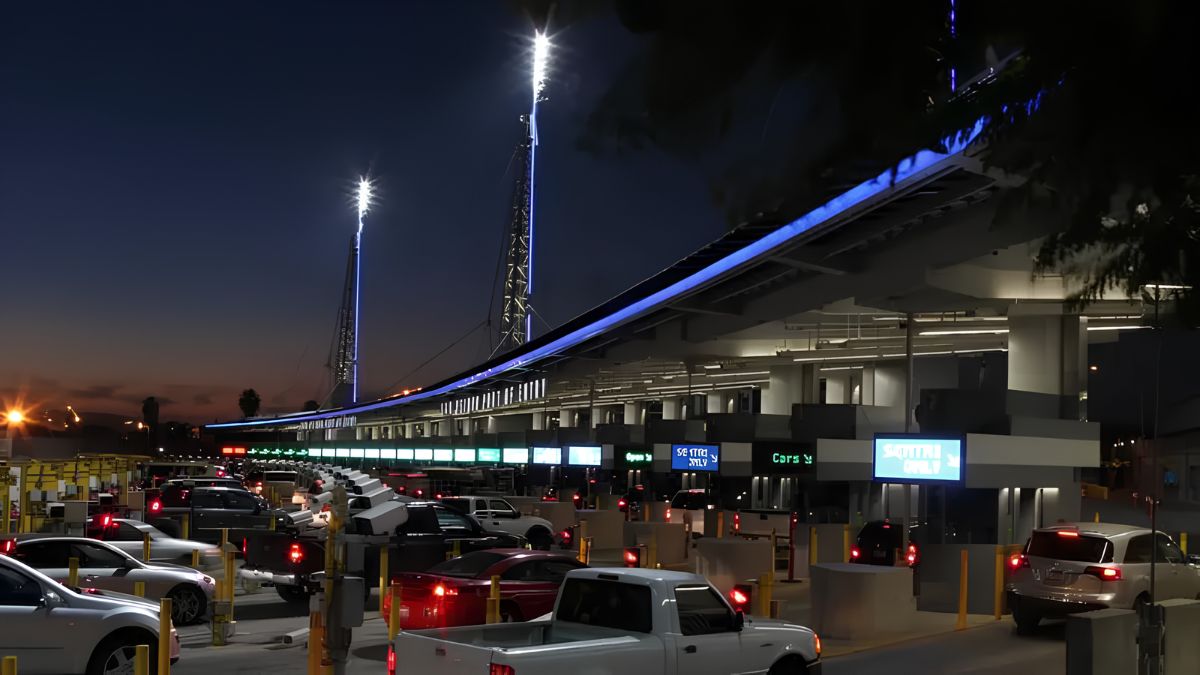 Cars and vehicles lined up at brightly illuminated border inspection booths during the evening.