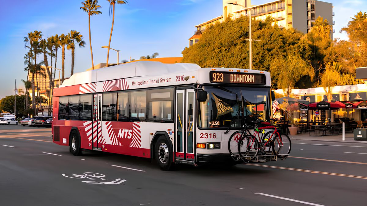 San Diego Metropolitan Transit System (MTS) bus with a bike rack on the front, traveling down a city street toward downtown.