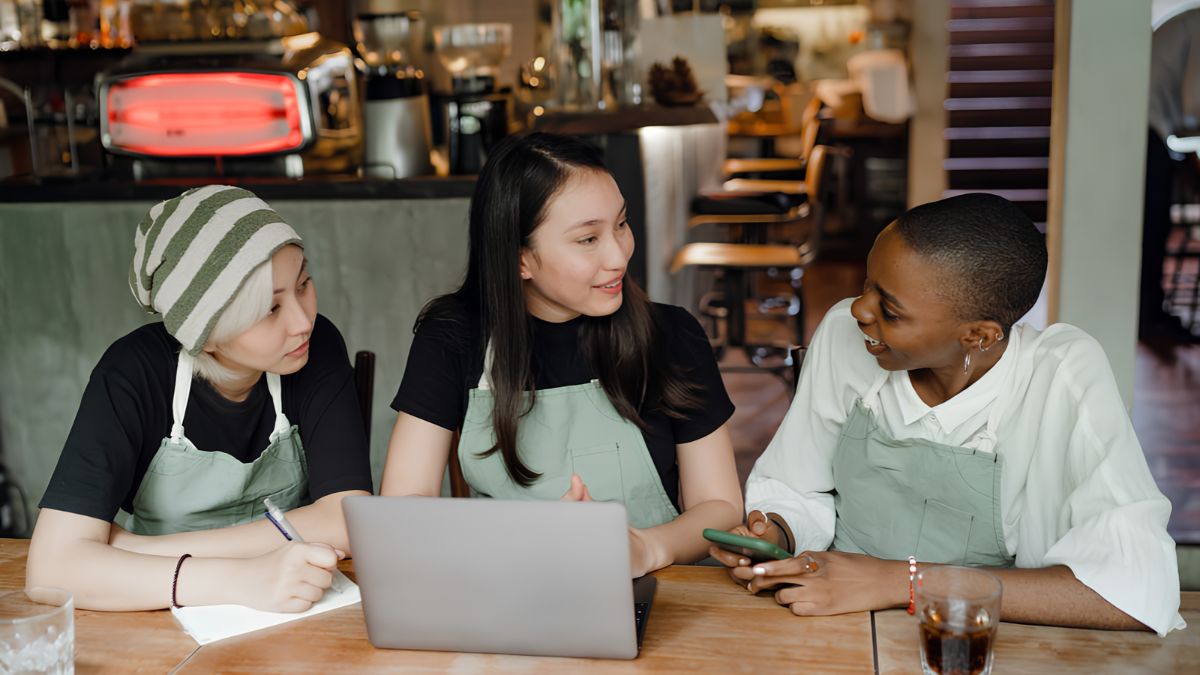 Three service workers in aprons collaborating around a laptop and smartphone to solve scheduling challenges for a San Ysidro business.