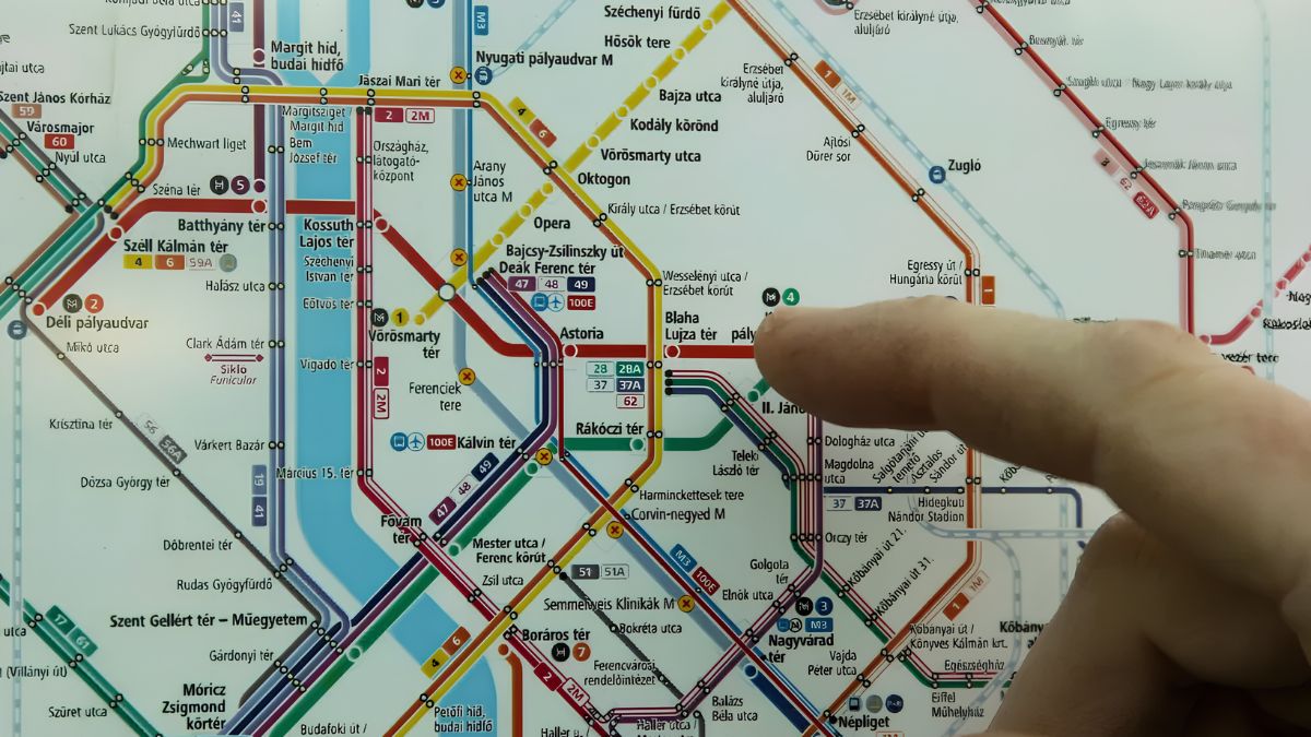 A close-up of a person pointing at a complex public transit map with color-coded lines and station names.