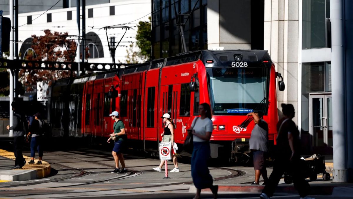 A red San Diego MTS trolley moving through an urban station, illustrating public transit routes from San Ysidro to San Diego.