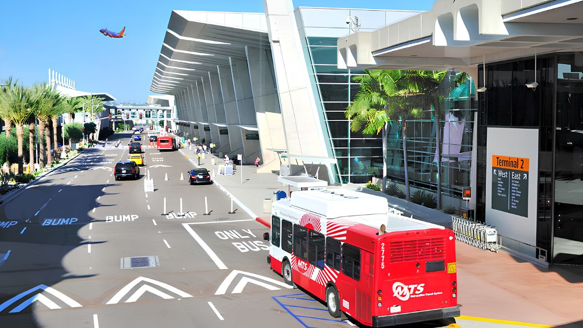 A red public transit bus driving past a modern terminal building during transfers